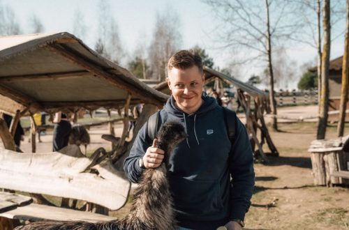 A cheerful young man interacting with an emu at a rustic outdoor farm setting, highlighting rural life.