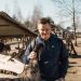 A cheerful young man interacting with an emu at a rustic outdoor farm setting, highlighting rural life.